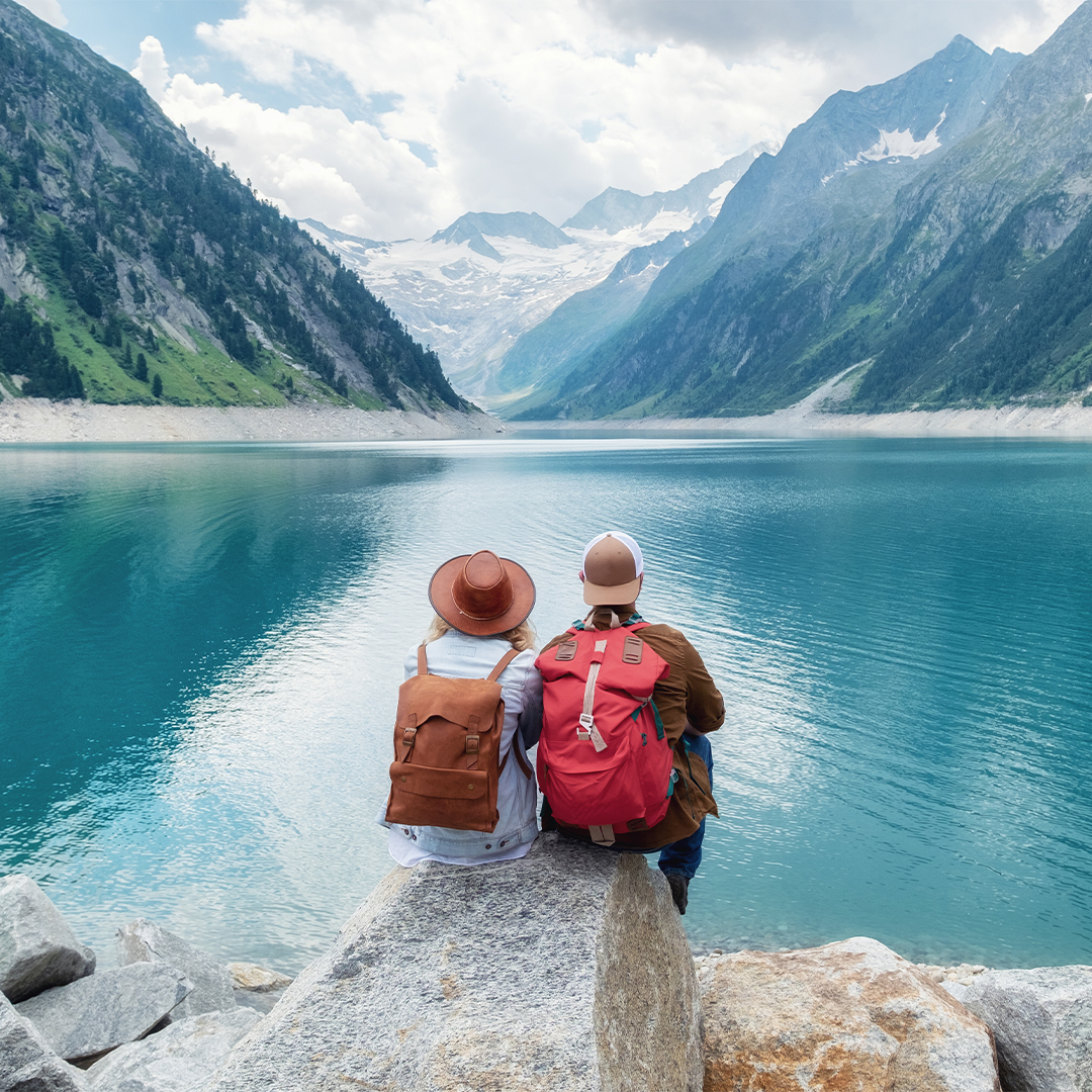 Couple wearing hats and backpacks looking out over a bright blue lake with mountains in the background- Odgers Executive Search Board Headhunters