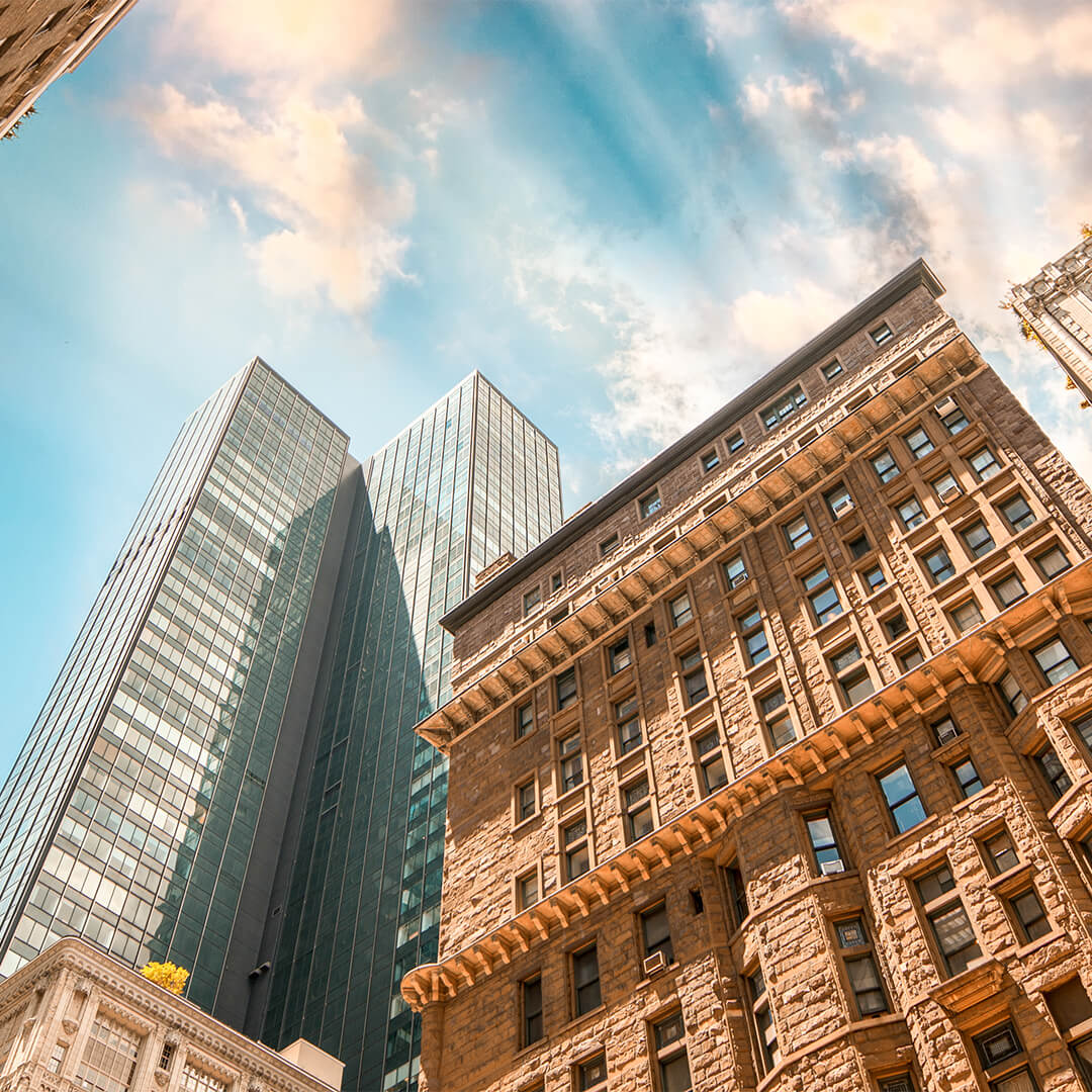 Looking up at classic brick building in front of two glass skyscrapers with blue sky in the background - Odgers Executive Search Board Headhunters